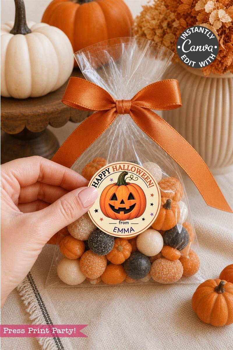 A hand holds a festive treat bag adorned with Pink Coquette Ghost Treat Bag Halloween Stickers and filled with orange, white, and black candies, tied up with an orange ribbon. A pumpkin tag reads “Happy Halloween from EMMA,” while mini pumpkins and fall décor surround the bag for a charming seasonal touch.