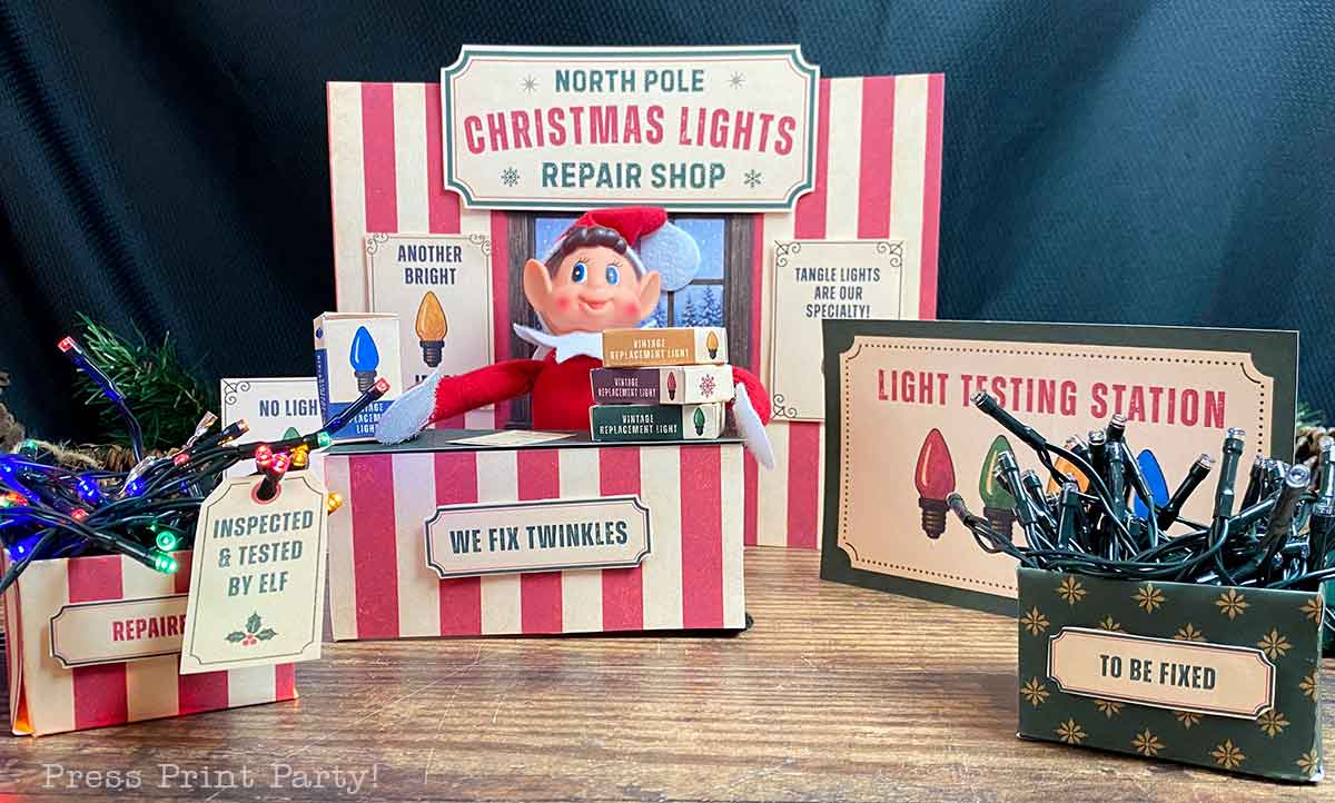 A miniature North Pole Christmas Lights Repair Shop playset featuring an elf at a desk, boxes for lights, and signs labeled βLight Testing Stationβ and βTo Be Fixed.β