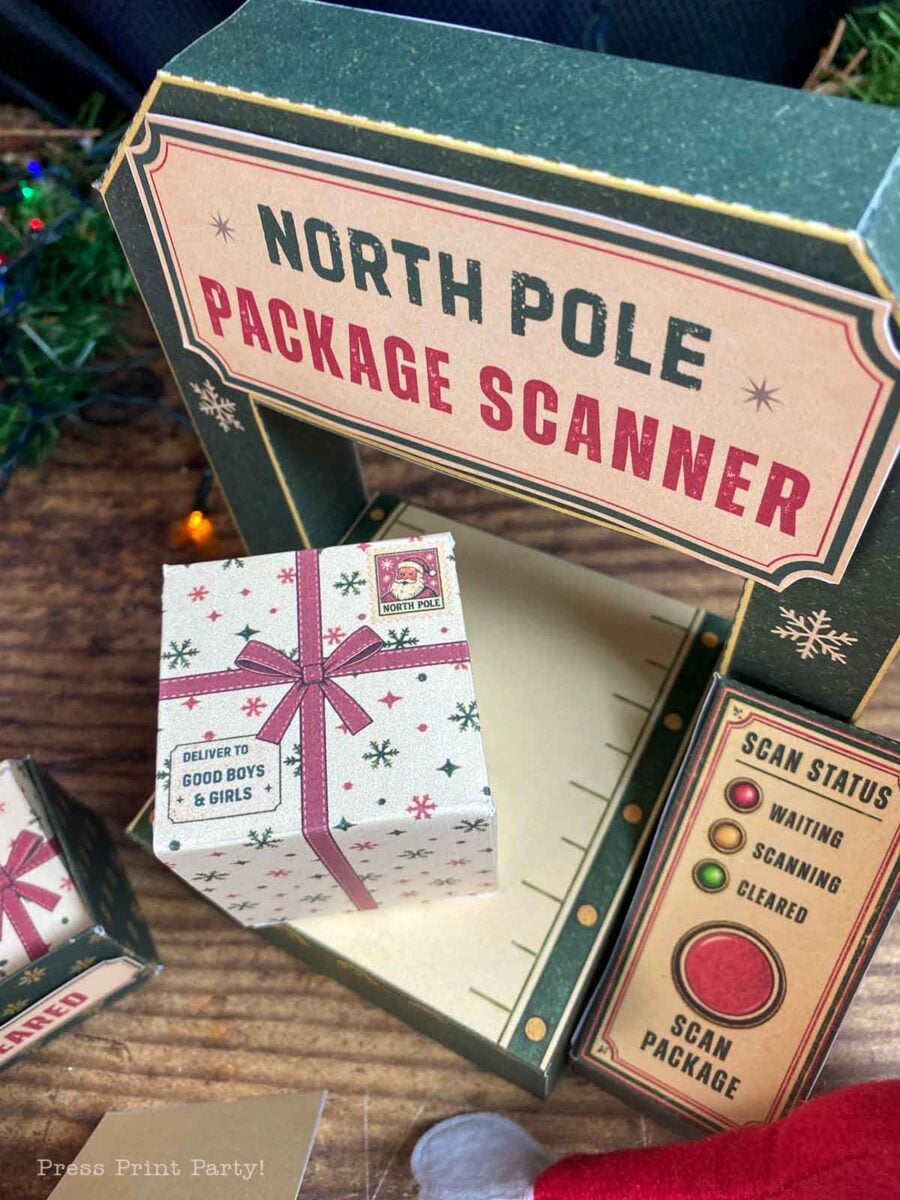 A toy North Pole package scanner with a small gift box sitting on the platform and a control panel with indicator lights.