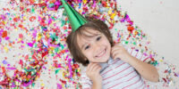 The secret to getting RSVPs to your kid's birthday party - smiling kid with birthday hat - Press Print Party!