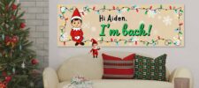 A festive living room with a decorated Christmas tree and a sofa with holiday pillows. Above the sofa is a banner with an elf, colorful lights, snowflakes, and the text "Hi Aiden, I'm back!.