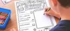 A child fills out a “My First Day of School” worksheet with crayons. The page has prompts for name, age, grade, favorite food, book, and a “Draw yourself” box. Colored crayons are in a blue container nearby.